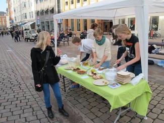 Veganske smagsprøver på store torv i Århus. Tre personer står ved en bod og gør smagsprøver klar.